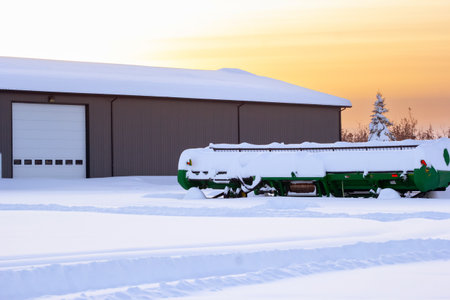 Spirit River, Alberta, Canada - December 27, 2025: John Deere green 635D Header - Draper is parked in the farm yard under high snow after heavy snowfall, orange sunset light and frosty winter.のeditorial素材
