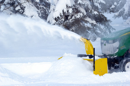 Spirit River, Alberta, Canada - December 27, 2025: John Deere compact tractor with a snowblower is plowing snow cleaning the driveway in the rural area. Snowy day in cold winter.のeditorial素材
