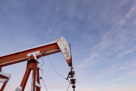 Oil pumpjack's horsehead against a soft pink winter sky at sunrise. Industrial energy production in...