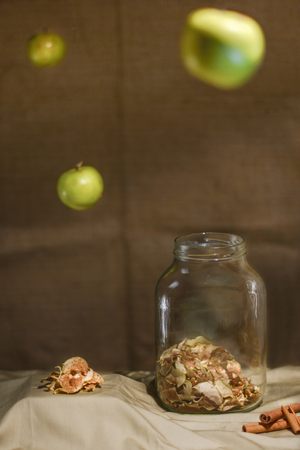 Dried apples with cinnamon. Arrangement with an old jar, cinnamon sticks and flying apples. Low key.の写真素材