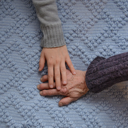 Granddaughter gently holding her hand over her grandmother’s hand. Hands are lying on a...