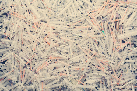 Medical waste. A pile of used plastic disposable syringes, a few detachable stainless steel needles,...