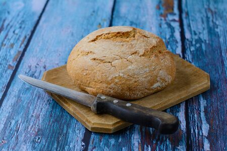 Fresh homemade leavened round bread on the cutting board. An old knife with a wooden handle is lying...