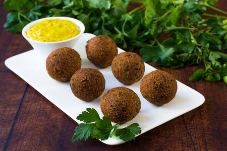 Vegan falafel placed on a white serving platter. Tahini sauce with turmeric powder and a handful of parsley leaves in a blurry background.の写真素材