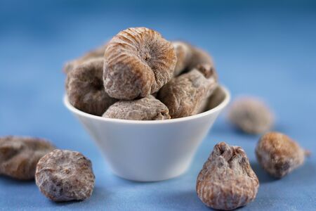 Sun-dried figs besprinkled with powdered sugar, in a white bowl. A few blurry figs are scattered around the bowl. Selective focus.の写真素材