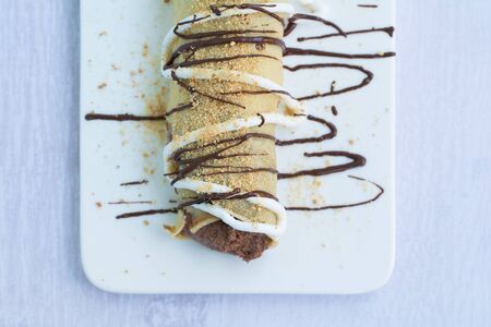 European pancake or palatschinke or palacinka with cocoa and crumb crust filling, decorated with chocolate topping, whipped cream and sprinkled with ground biscuits, lying on a white plate.の写真素材