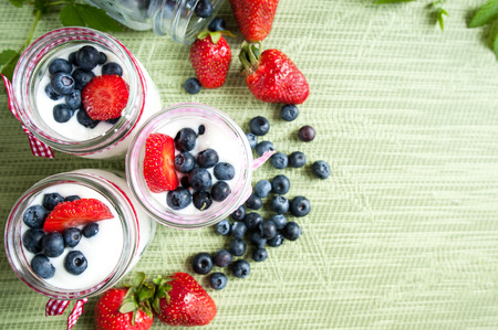 Three jars of yogurt with blueberries and strawberries, square. Berries of blueberries and strawberries are scattered on the table. Cooking, healthy food, food packagingの写真素材