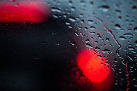 Drops of rain on the glass, in the defocus of the red lights of cars. Background for illustration of a road situation, weatherの写真素材