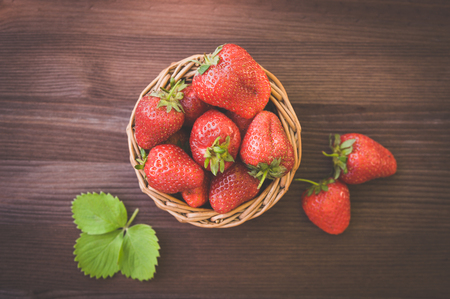Juicy strawberries in a wicker basket, on a wooden table, against the backdrop of a beautiful background green garden. Cooking, food industry, restaurant business, gardening, proper nutrition の写真素材