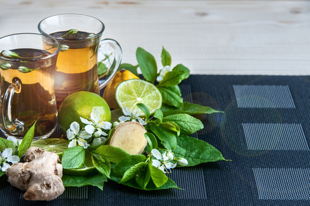 Tea background . Tea in transparent mugs with lemon, lemons, limes, mint, cherry blossoms. Stylish, colorful background. Food industry, tea packing, restaurant businessの写真素材