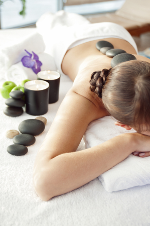 Stone treatment. Top view of beautiful young woman lying on front with spa stones on her back.  Beauty treatment concept.の写真素材