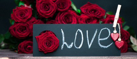 Concept Valentine day, the word love written in chalk on a plate on a background of a pile of red roses. Stylish love conceptの写真素材