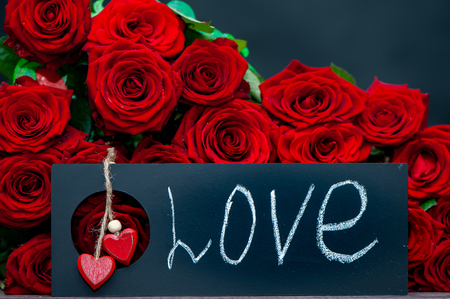 Concept Valentine day, the word love written in chalk on a plate on a background of a pile of red roses. Stylish love conceptの写真素材