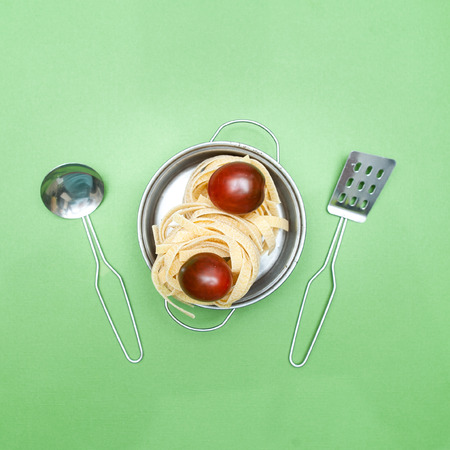 Dry pasta  tagliatelle  and cherry  on a green background, stylish concept, flat layの写真素材
