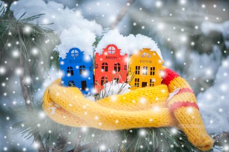Toy houses is wrapped in a warm scarf, it's snowing on a natural natural background of a real fir in the snow, toned. Concept of winter, Christmas, new year,
 warm, cozy in the cityの写真素材