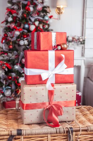 Boxes tied with ribbons one on one against the background of a Christmas tree in red colors. Symbol of congratulations and gifts for the New Year and Christmas.の写真素材