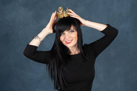Very beautiful girl with with a very nice face and a smile trying on the crown. Concept queen, a princess, a gorgeous woman. Studio portrait on a monochrome blue, trendy shabby backgroundの写真素材