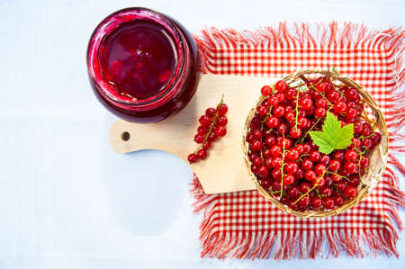 Red and ripe red currants in a straw bowl and jars of berry jam, space for text, flat lay. Harvest and cooking themeの写真素材
