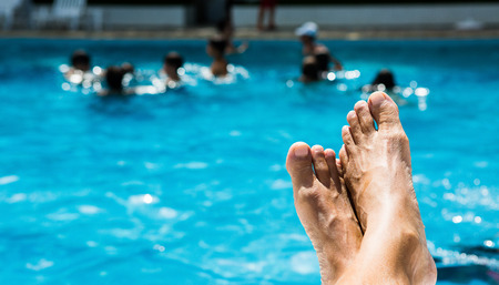 Resting by the pool, with children playing in the background.の写真素材