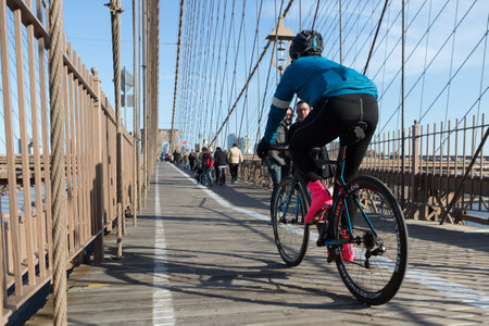 Cyclist cycling on the Brooklyn Bridge bike path on a sunny day alongside several tourists.のeditorial素材