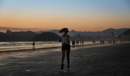 Santos, Brazil. December 05,2018. Girl running on the edge of Santos beach during a beautiful sunset.のeditorial素材