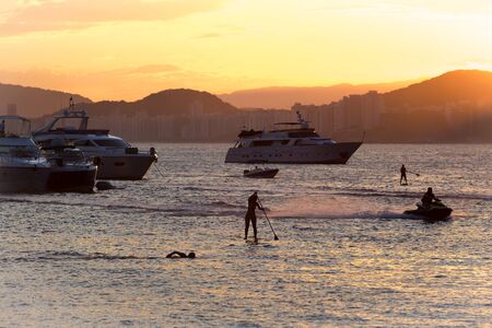 Guaruja, Brazil. Mars 26, 2016. Sunset at Enseada beach with people playing various sports and...
