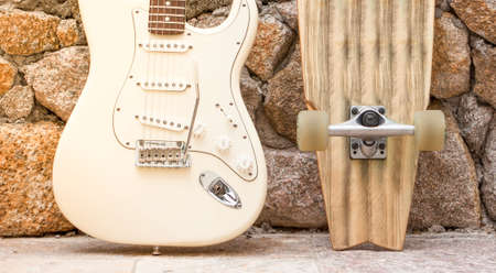 Body of a guitar and skateboard leaning against a stone wall.の写真素材