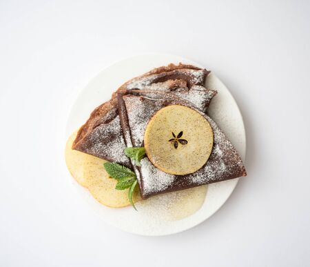 chocolate protein pancakes with apples and icing sugar on a white plateの写真素材