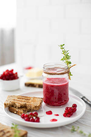 breakfast with redcurrant jam, rye bread and butter in white plate