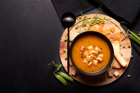carrot and green pea puree soup in a black bowl, top viewの写真素材
