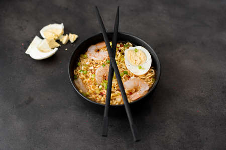 egg noodles with shrimps, green onions and spices in black bowlの写真素材