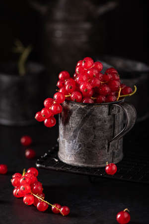 red ripe bunches of currants in an iron mug on a black background