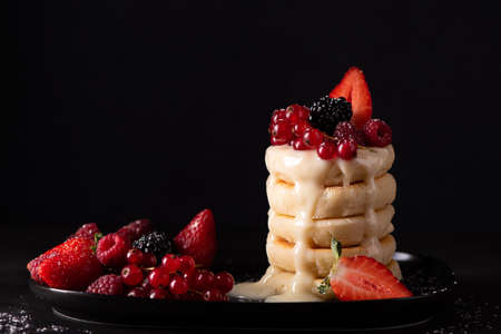 cottage cheese pancakes with fresh berries and condensed milk on a black dish