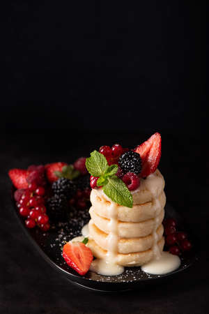 cottage cheese pancakes with fresh berries and condensed milk on a black dish