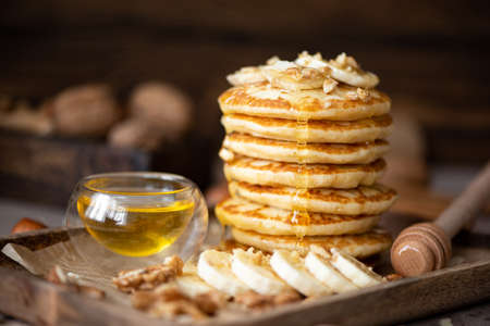 small pancakes with banana, walnuts and honey on a wooden trayの写真素材