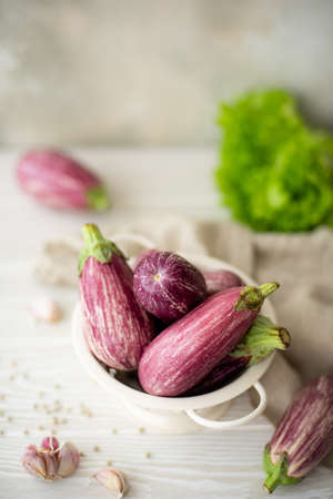 small fresh striped eggplant with greens on a white tableの写真素材