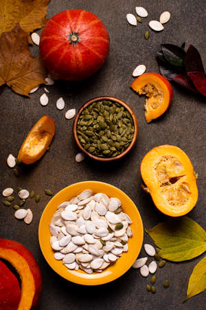 small orange pumpkins and pumpkin seeds on a dark table, top viewの写真素材