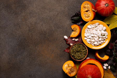 small orange pumpkins and pumpkin seeds on a dark table, top viewの写真素材