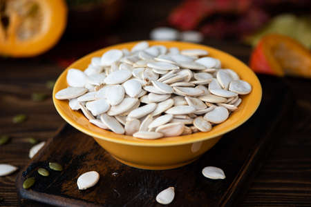 white dried pumpkin seeds in a yellow plate on a wooden tableの写真素材