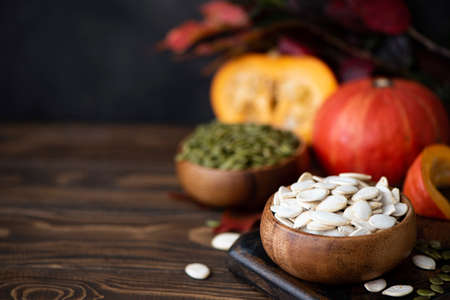 white dried pumpkin seeds and small pumpkins on a wooden tableの写真素材