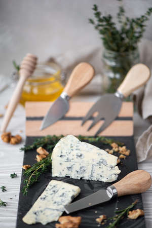 a piece of dor blue cheese with thyme and walnuts on a cheese board with knivesの写真素材