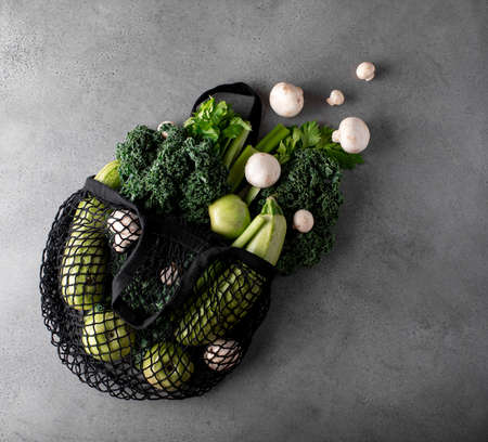 green vegetables and fruits in an eco bag on a gray table, top viewの写真素材