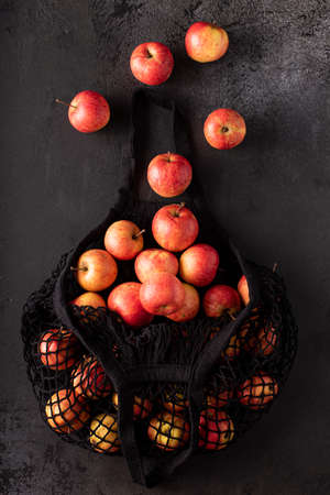 red garden apples in a black eco bag on a dark table, top view