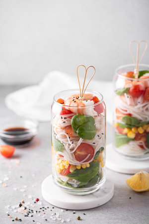 rice noodles with shrimps and vegetables in a glass jar on a white table, top viewの写真素材