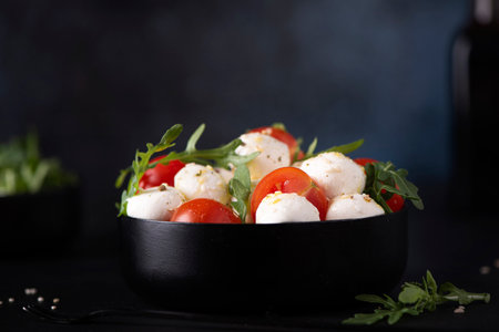 mozzarella salad of cherry tomatoes and arugula seasoned with olive oil in a black bowl, close upの写真素材