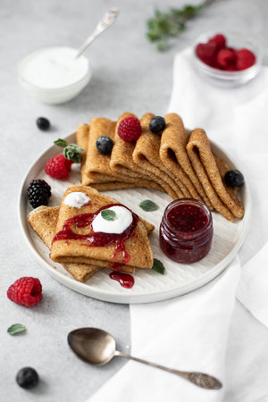 thin sweet pancakes with fresh berries and jam on a gray plate, close-up
