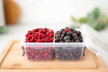 frozen cranberries and black currants in plastic containers, close-up