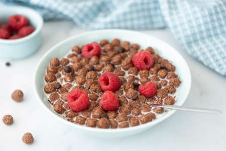 chocolate flakes balls with milk and raspberries in a blue bowl, close-up