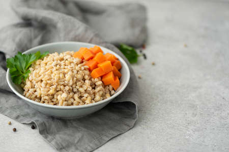boiled pearl barley with butter and carrots in a gray plate, close-upの写真素材