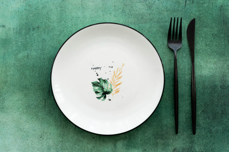 white patterned ceramic plate with fork and knife on green table, top view